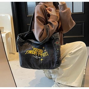 Détail de broderie jaune sur un grand sac cabas en denim noir lavé au style vintage
