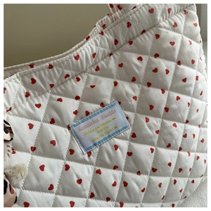 Détail d'un sac cabas matelassé blanc avec motifs cœurs rouges et étiquette bleue
