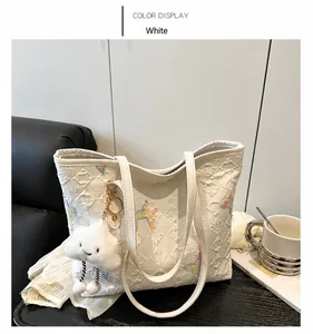 Detail van witte gewatteerde draagtas met vlinderborduurwerk en wolk pluche bedeltje