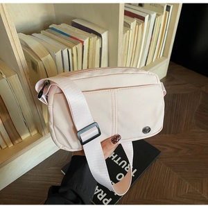 Gros plan d'un sac bandoulière en nylon rose clair avec sangle réglable et logo métal