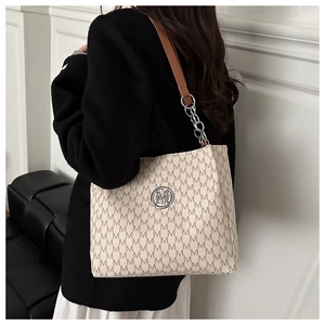 Close-up of beige tote bag featuring brown M-letter print and silver metal logo detail