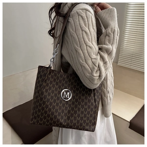 Detail of a large brown tote bag with M-pattern and silver chain strap on a shoulder