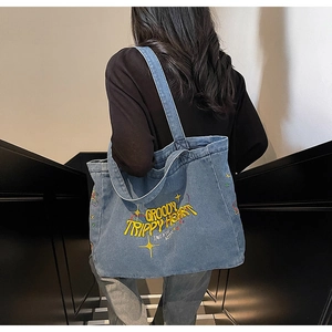 Vue détaillée du sac cabas en denim délavé avec broderie jaune sur tissu bleu