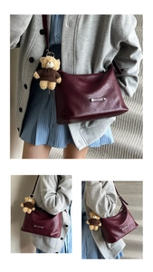 Detail of burgundy leather tote bag featuring a silver plaque and brown teddy bear charm