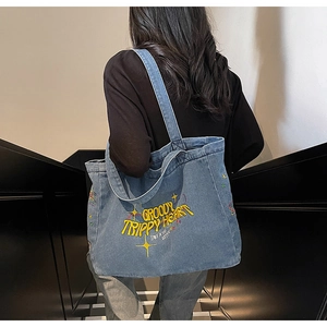 Sac fourre-tout en jean bleu avec broderie jaune porté par un mannequin en extérieur