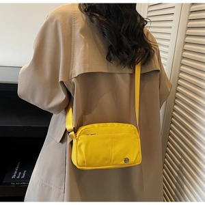 Vue arrière d'un sac bandoulière en toile jaune à poches multiples porté sur un manteau beige