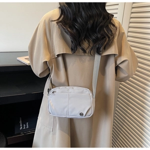 Dettaglio vista posteriore della borsa a tracolla in nylon grigio chiaro su trench kaki
