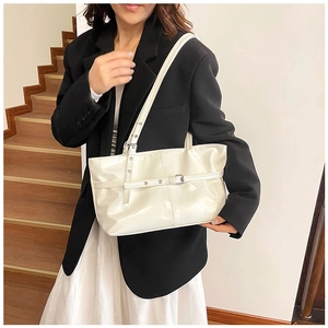 Detail shot of a glossy cream underarm tote bag with metallic buckle strap decoration