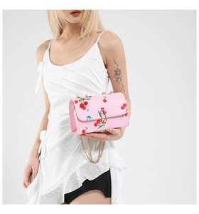 Detail of pink cherry print shoulder bag with gold chain strap on a white dress