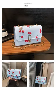 Detail of light blue crossbody bag featuring red cherry prints and gold snake chain strap
