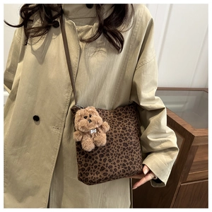 Bolso de lona con estampado de leopardo y colgante de oso sobre una gabardina beige