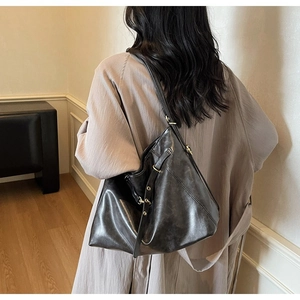 Side view of black glossy leather tote bag with gold ring buckle on model wearing trench coat