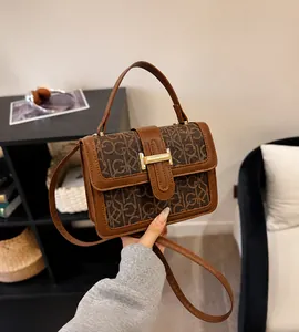 Detail of a brown leather handbag with letter pattern and golden H-shaped buckle