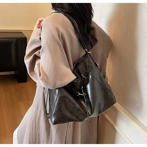 Detail of a large black glossy leather tote bag with gold hardware and side drawstrings