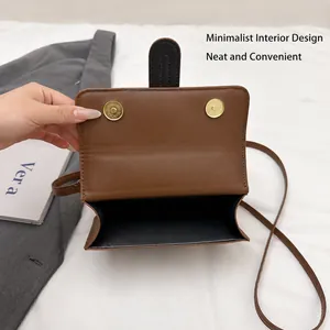 Detail of a brown leather crossbody bag featuring dual gold magnetic closures and interior