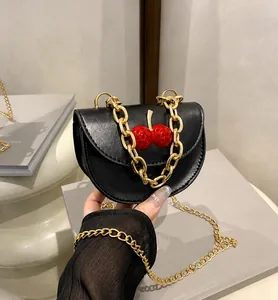 Detalle de mini bolso bandolera negro con decoración de cerezas y cadena dorada