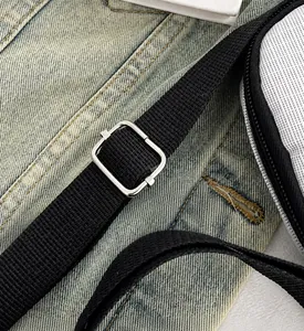 Detail of adjustable silver buckle on black woven shoulder strap with denim accents