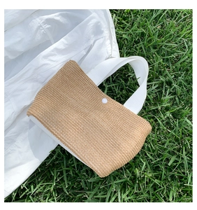 Detail of woven straw handbag with white fabric handles on green grass background
