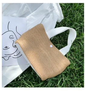 Detail of straw woven tote bag with white canvas handles on a sunny lawn background