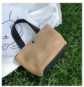 Detailed close-up of woven straw handbag with black leather handles on grass