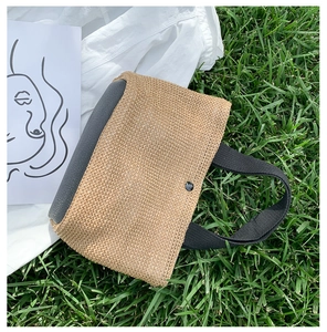 Detailed close-up of woven straw handbag with gray leather panels on green grass