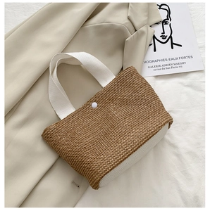 Detail of hand-woven straw bag with white handles and secure snap button closure