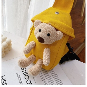 Detail of yellow canvas crossbody bag featuring a 3D plush teddy bear and metal eyelet