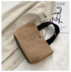 Detailed top view of straw tote bag with black handles on a beige fabric background