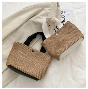Close-up of woven straw beach bags with contrast black and white handles and button closure