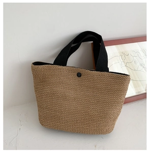 Close-up of woven straw tote bag with black canvas straps and a snap button closure