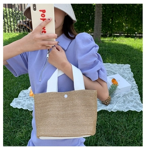 Detail of summer straw tote bag featuring white canvas handles and natural woven texture