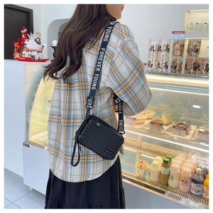 Close-up of black glossy mini suitcase crossbody bag with Forever Young strap