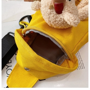 Close-up of yellow canvas bag with metal zipper and cream plush bear pendant charm