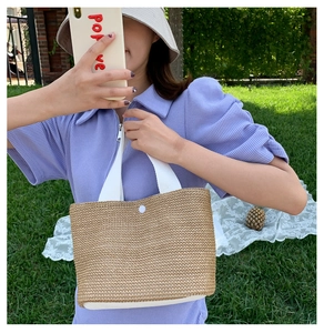 Detail of straw woven tote with white canvas handles and snap button on a grassy background