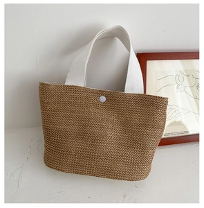 Detail of hand-woven straw tote with white cotton handles and a white snap button closure