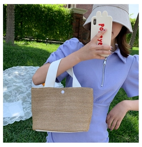 Detailed macro of handmade straw tote with white woven handles and single snap button closure