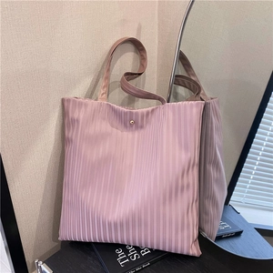 Pink pleated large capacity tote bag displayed on a book in a minimalist interior setting