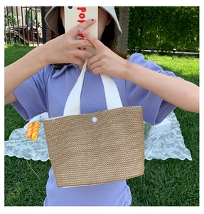 Detail of summer straw woven tote bag featuring white canvas handles and snap button closure