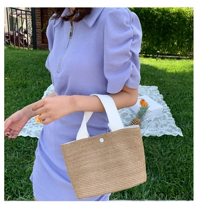 Detail of woven straw handbag with white canvas handles and snap closure for beach