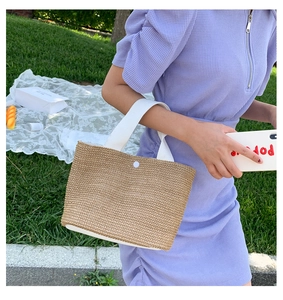Detail of woven straw handbag with white canvas handles held by model in outdoor setting