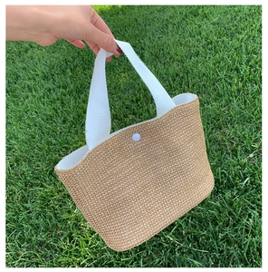 Close-up of hand-woven straw tote bag with white canvas handles and snap button closure