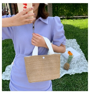 Detail of summer straw beach bag with canvas handles on green grass picnic setting