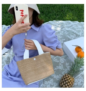 Detail of woven straw handbag with white canvas handles and snap closure on green grass