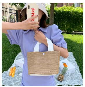 Detail of summer woven straw handbag with white canvas handles and button closure