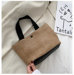 Detail of woven straw tote bag with black leather base and fabric handles on soft cloth