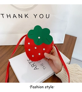 Close-up of a red strawberry shaped kids crossbody bag with white rhinestones on art books