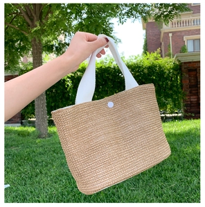 Detail of hand-woven straw tote with white canvas handles and snap closure button