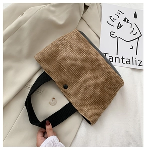Detail of straw woven tote bag featuring black canvas handles and secure snap button closure