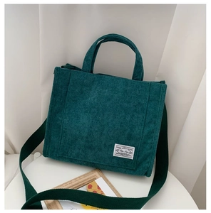 Detailaufnahme einer dunkelgrünen Cord-Tasche mit gewebtem Schultergurt auf weißem Tisch