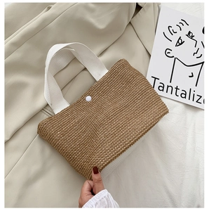 Close-up of woven straw bag showing white canvas handles and snap button closure